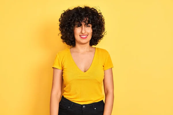 年轻的阿拉伯妇女卷发穿着T恤站在孤立的黄色背景眨眼看相机性感的表情 欢快和快乐的脸 — 图库照片