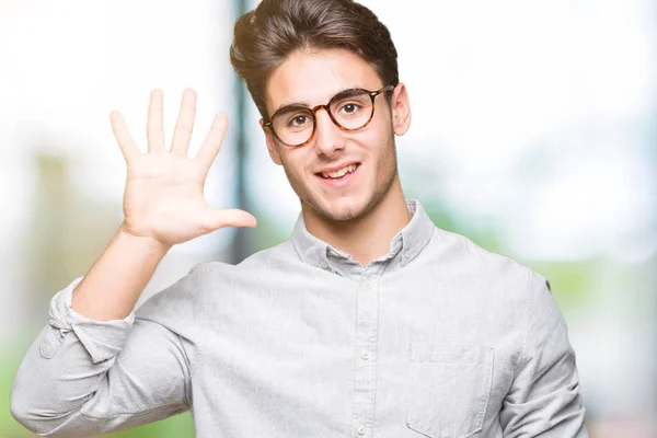 若いハンサムな男で眼鏡をかけて分離を示す背景と自信を持って 幸せな笑みを浮かべて 指で上向きナンバーファイブ — ストック写真