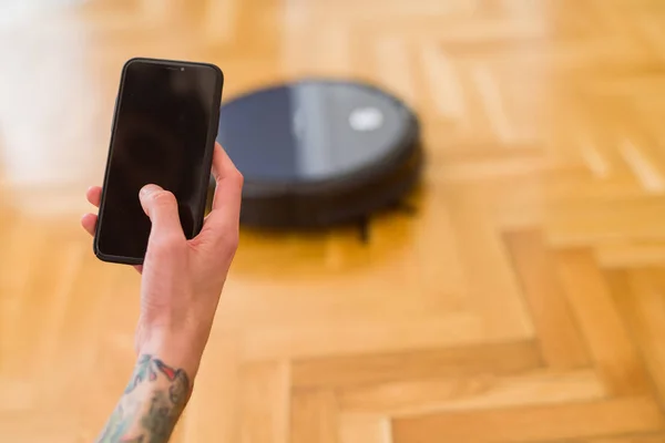 Gros plan des mains de l'homme contrôlant l'aspirateur automatique à l'aide — Photo