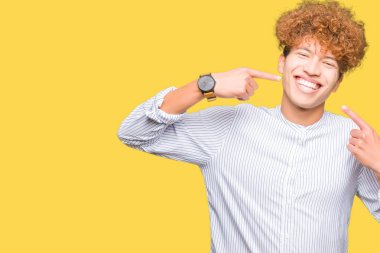 Kendinden emin gösterilen ve işaret parmakları diş ve ağız ile gülümseyen şık gömlek giymiş afro saçlı Genç yakışıklı iş adamı. Sağlık kavramı.