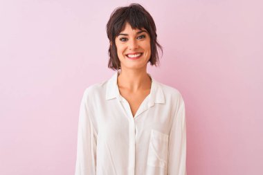 Yüzünde mutlu ve serin bir gülümseme ile izole pembe arka plan üzerinde duran beyaz gömlek giyen genç güzel kadın. Şanslı kişi.