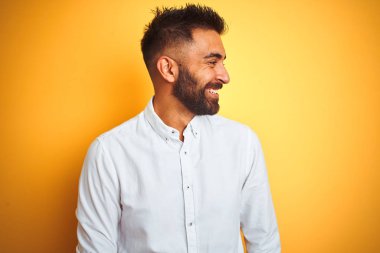 Beyaz zarif gömlek giyen Hintli işadamı izole sarı arka plan üzerinde duran yüzünde gülümseme, doğal ifade ile yan bakıyor. Gülmekten emin.