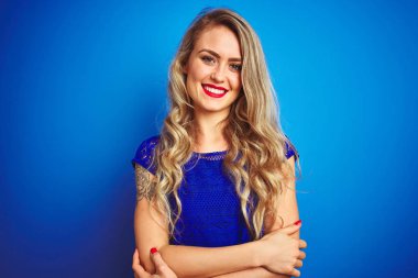 Mavi izole arka plan üzerinde duran genç güzel kadın kamera bakarak çapraz kolları ile gülümseyen mutlu yüz. Pozitif kişi.