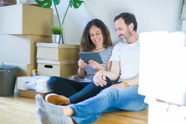 Orta yaş yaşlı çift ayakta mutlu bir yüz ile tablet kullanarak yeni bir eve hareket ve dişleri gösteren kendinden emin bir gülümseme ile gülümseyerek