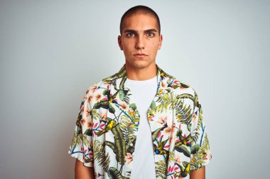Tatilde beyaz arka plan üzerinde Hawaii gömlek giyen genç yakışıklı adam yüzünde ciddi ifade ile rahat. Kameraya basit ve doğal bir bakış.