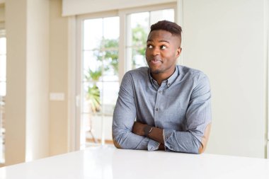 Yakışıklı afro-amerikan adam beyaz masada gülümseyerek yan bakıyor ve düşünme uzak bakıyor.