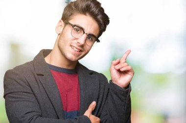 Kameraya bakarak yan el ve parmak ile işaret yüzünde kocaman bir gülümseme ile izole arka plan üzerinde gözlük takan genç yakışıklı zarif adam.
