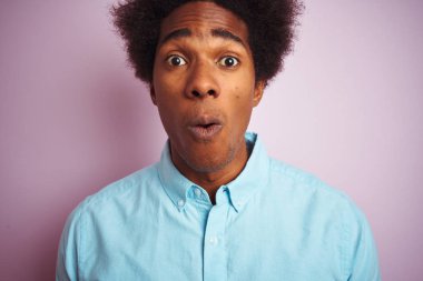 Afro saçlı mavi gömlek giyen genç amerikalı adam izole pembe arka plan üzerinde duran sürpriz bir yüz ile şok korkmuş, korku ifade korku ve heyecanlı