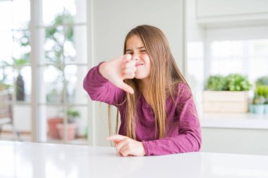 Beyaz masada güzel genç kız çocuk mutsuz ve kızgın görünümlü reddedilme ve başparmak aşağı jest ile olumsuz gösteren. Kötü ifade.