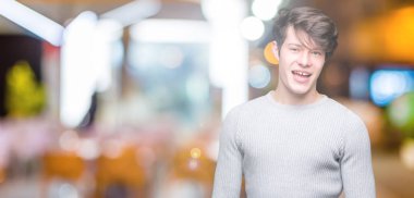 Seksi bir ifadeyle, neşeli ve mutlu yüzünü kameraya bakarak göz kırpıyor izole arka plan üzerinde kış kazak giyen genç yakışıklı adam.