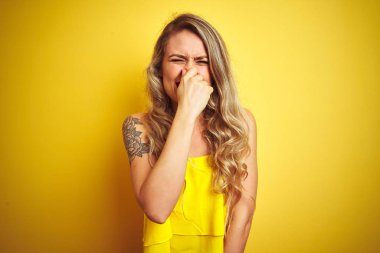 Genç attactive kadın sarı izole arka plan üzerinde duran t-shirt giyen bir şey kokulu ve, dayanılmaz koku, burun parmakları ile nefes tutan kokuyor. Kötü kokular kavramı.