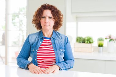 Evde kot ceket giyen kıvırcık saçlı orta yaş yaşlı kadın şüpheci ve sinirli, sorun nedeniyle üzgün kaşlarını çatma. Negatif kişi.