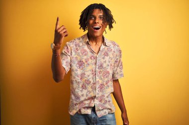 Başarılı bir fikir ile parmak işaret izole sarı arka plan üzerinde çiçek gömlek giyen tatilde dreadlocks ile Afro adam. Çıktı ve mutlu. Bir numara.