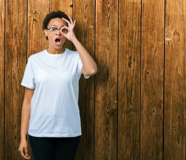 Güzel genç Afro-Amerikan kadın Tamam jest yapıyor izole arka plan üzerinde gözlük sürpriz yüz, göz parmaklarının arasından seyir ile şok. İmansız ifade.