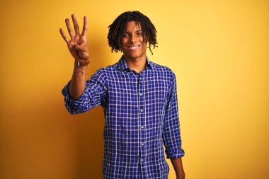 Kendinden emin ve mutlu gülümserken izole sarı arka plan üzerinde duran ve parmakları ile işaret eden rahat gömlek giyen dreadlocks ile Afro adam.