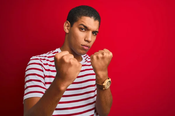年轻英俊的阿拉伯男子穿着条纹T恤在孤立的红色背景准备与拳头防御手势战斗 愤怒和沮丧的脸 害怕问题 — 图库照片
