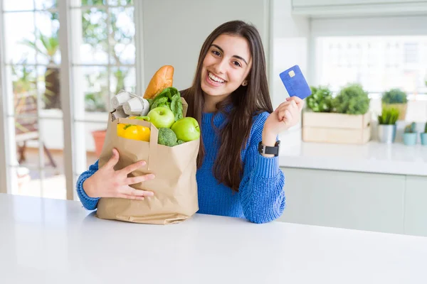 Mujer joven sosteniendo una bolsa de papel llena de alimentos frescos y mostrar — Foto de Stock