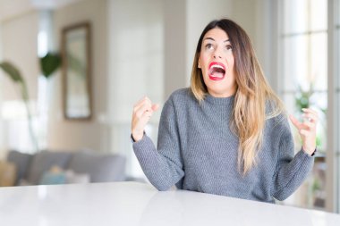 Evde çılgın ve kızgın bağırarak ve agresif ifade ve silah kaldırdı bağırmaya kış kazak giyen genç güzel kadın. Hayal kırıklığı kavramı.