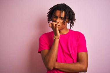 Afro amerikan adam dreadlocks t-shirt izole pembe arka plan üzerinde duran görünümlü stresli ve ağız tırnak ısırma elleri ile sinir. Anksiyete sorunu.