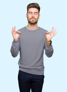 Çizgili süveter dinlenmek giydiği ve gözleri ile gülümseyen yakışıklı delikanlı parmak ile meditasyon jest yapıyor kapalı. Yoga kavramı.