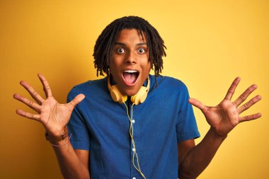 Afro amerikan adam dreadlocks izole sarı arka plan üzerinde kulaklık giyen deli kutluyor ve silah kaldırdı ve açık gözleri heyecan çığlık ile başarı için hayran. Kazanan kavramı
