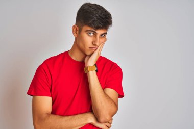 İzole beyaz arka plan üzerinde duran kırmızı t-shirt giyen genç hintli adam yorgun görünümlü ve çapraz kolları ile depresyon sorunları ile sıkılmış düşünme.