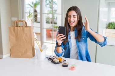 Akıllı telefon kullanarak uygulamadan yemek teslimatı sipariş eden güzel genç kadın çok mutlu ve heyecanlı, zaferi büyük bir gülümsemeyle çığlık atarak ve ellerini kaldırarak zaferi kutlayan kazanan ifade