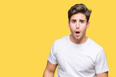 Yakışıklı delikanlı beyaz giyen şüpheci ve alaycı, t-shirt üzerine şok karşısında izole arka plan açık ağız ile şaşırttı.