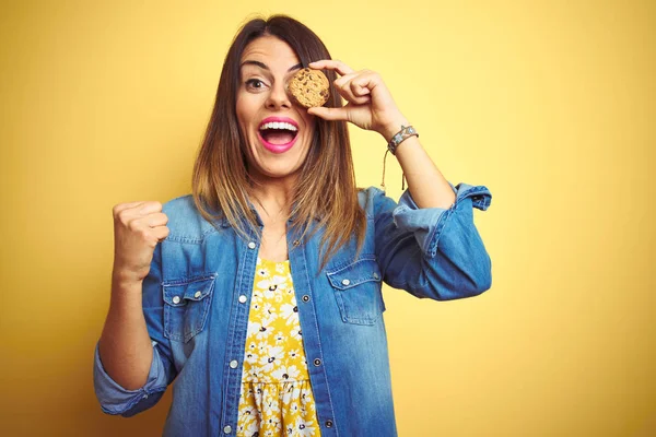 Young Beautiful Woman Eating Chocolate Chips Cookie Yellow Background Screaming — Stock Photo, Image