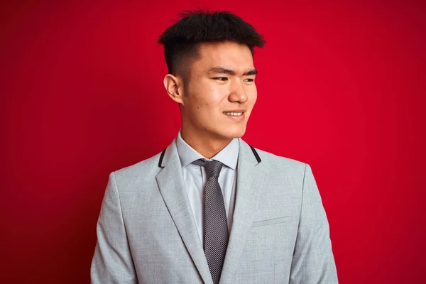灰色のジャケットとネクタイを着たアジアの中国人ビジネスマンは 顔に笑顔で横を向いて 孤立した赤い背景の上に立って 自然な表情 自信を持って笑う — ストック写真