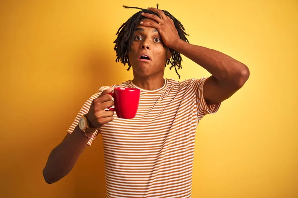Afro american man with dreadlocks drinking a cup of coffee over isolated yellow background stressed with hand on head, shocked with shame and surprise face, angry and frustrated. Fear and upset for mistake.