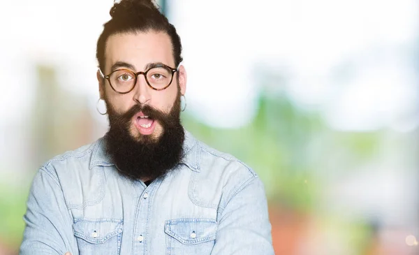 Young hipster man with long hair and beard wearing glasses afraid and shocked with surprise expression, fear and excited face.