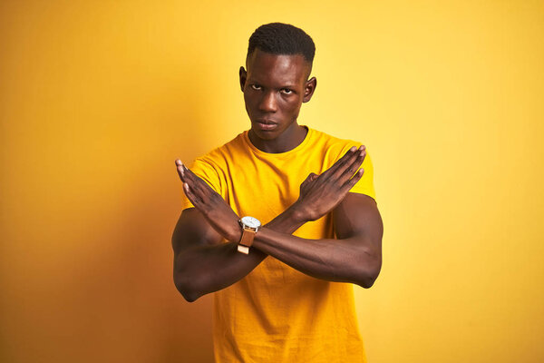 Young african american man wearing casual t-shirt standing over isolated yellow background Rejection expression crossing arms doing negative sign, angry face