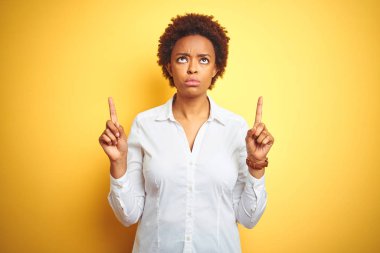 Izole sarı arka plan üzerinde Afrikalı-Amerikalı iş kadını üzgün ve üzgün görünümlü kadar işaret, parmakları ile yön gösteren, mutsuz ve depresif.