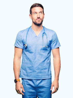 Yakışıklı doktor erkek görünümlü yan ve dik dik bakma uzağa düşünce gülümseyen izole arka plan üzerinde tıbbi üniforma.