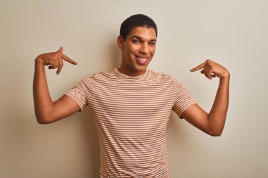 Genç yakışıklı arap adam izole beyaz arka plan üzerinde çizgili t-shirt giyen yüzünde gülümseme ile emin görünümlü, parmakları gururlu ve mutlu kendini işaret.