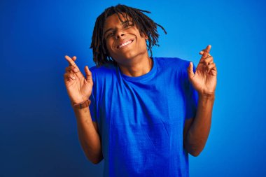 Izole mavi arka plan gesturing parmak üzerinde duran t-shirt giyen dreadlocks giyen Afro Amerikan adam umut ve gözleri kapalı gülümseyerek geçti. Şans ve batıl kavram.