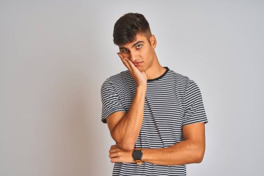 İzole beyaz arka plan üzerinde duran lacivert çizgili t-shirt giyen genç hintli adam yorgun görünümlü ve çapraz kolları ile depresyon sorunları ile sıkılmış düşünme.