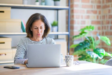Orta yaş kıdemli kadın ciddi düşünme akıllı yüz üzerinde güvenli bir ifade ile bilgisayar laptop kullanarak evde çalışma masasında oturan