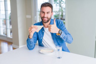 Yakışıklı adam ok işareti yapıyor büyük bir gülümseme ile mutlu sağlıklı sandviç yeme, parmakları ile başparmak, mükemmel işareti