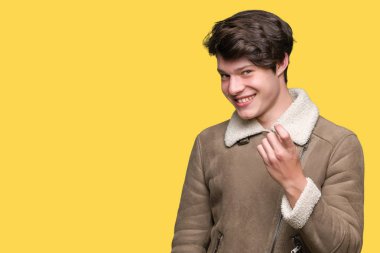 Genç yakışıklı adam giyen kış ceket izole arka plan üzerinde Beckoning gel burada mutlu ve gülümseyerek el davet ile jest