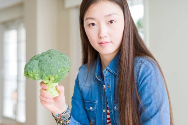 Güzel Asyalı kadın ciddi düşünme akıllı yüz üzerinde emin bir ifade ile Yeşil taze brokoli yeme