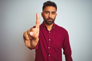 Kırmızı zarif gömlek giyen genç hintli adam izole gri arka plan üzerinde duran parmak yukarı ve kızgın ifade ile işaret, hiçbir jest gösteren