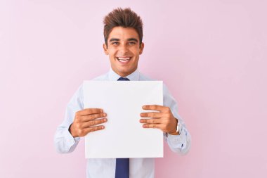 Genç yakışıklı işadamı mutlu bir yüz ayakta ve dişleri gösteren kendinden emin bir gülümseme ile gülümseyerek izole pembe arka plan üzerinde duran afiş tutan