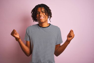 Dreadlocks giyen dreadlocks ile afro adam izole pembe arka plan üzerinde duran kollu kaldırdı ve açık gözleri ile başarı için şaşırttı ve şaşırttı. Kazanan kavramı.