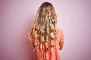 Pembe izole arka plan üzerinde duran t-shirt giyen genç güzel kadın çapraz kolları ile geriye bakarak ayakta