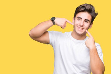 Kendinden emin gösterilen ve işaret parmakları diş ve ağız ile gülümseyen izole arka plan üzerinde beyaz t-shirt giyen genç yakışıklı adam. Sağlık kavramı.