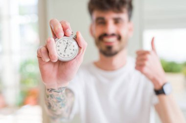 Büyük bir gülümseme ok işareti yapıyor, parmaklarla başparmak, mükemmel işareti ile kronometre mutlu tutarak genç adam