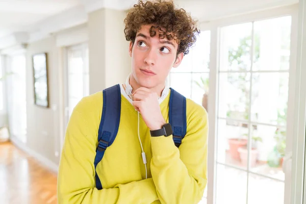ヘッドフォンとバックパックを身に着けている若い学生の男は ペンシブな表情を考えてあごに手を当て 思慮深い顔で微笑む 疑いの概念 — ストック写真