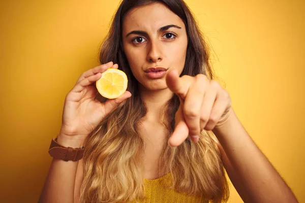 カメラに指で指で指を指し示す黄色の孤立した背景の上に半分のレモンを保持している若い美しい女性は 手のサイン 正面から肯定的で自信のあるジェスチャー — ストック写真